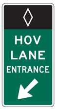 A highway sign: At the top, a white diamond in outline on a black field; underneath that, the words HOV LANE Entrance in white lettering on a green field, with a white left-and-downward-pointing arrow